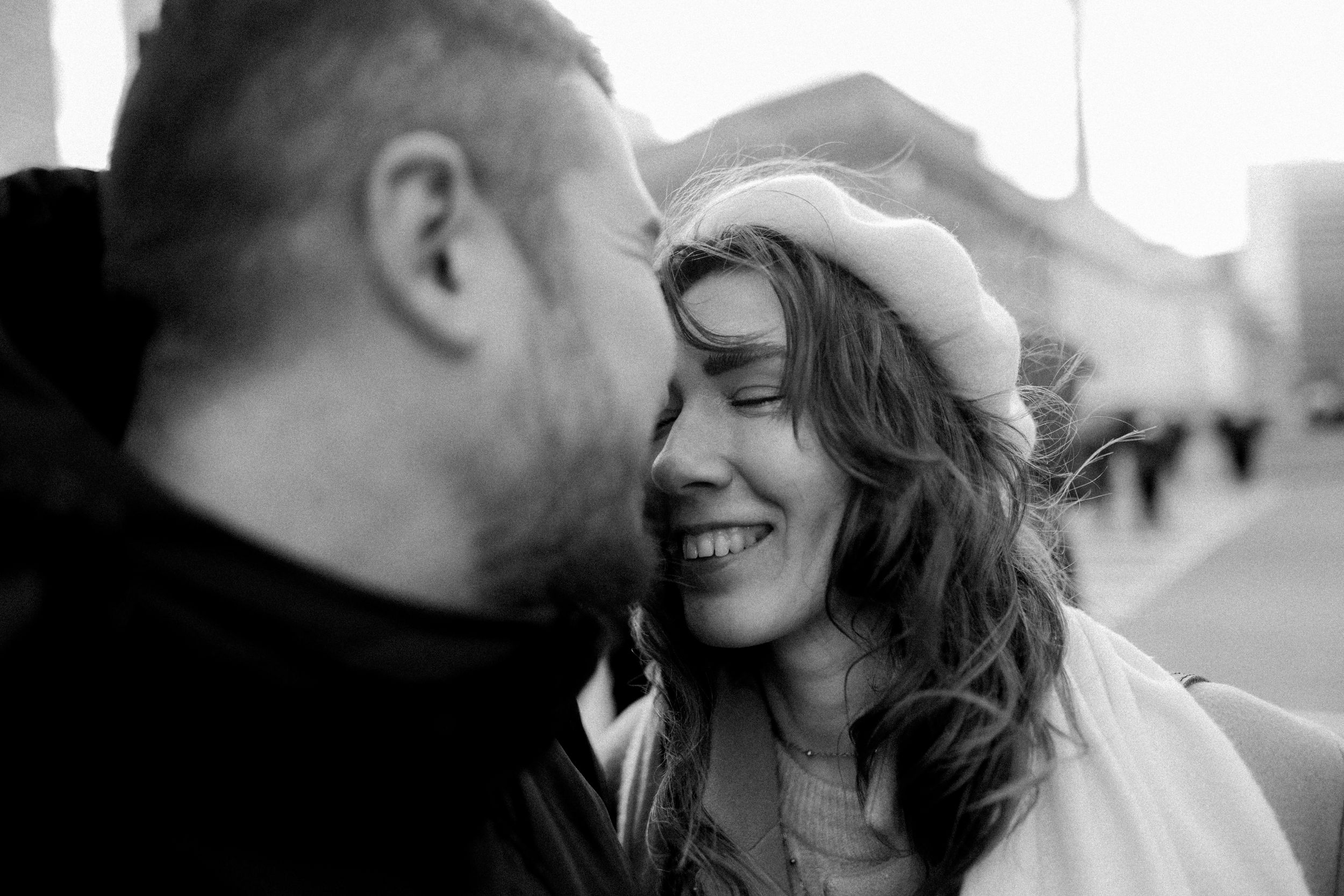A close-up black and white photo capturing a tender moment between two people on a city street.