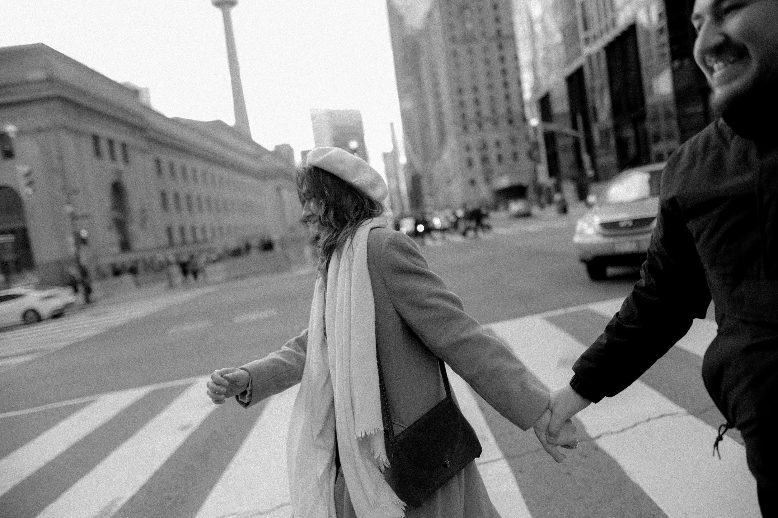 A black and white photo showing people crossing a street with the CN Tower visible in the distance.