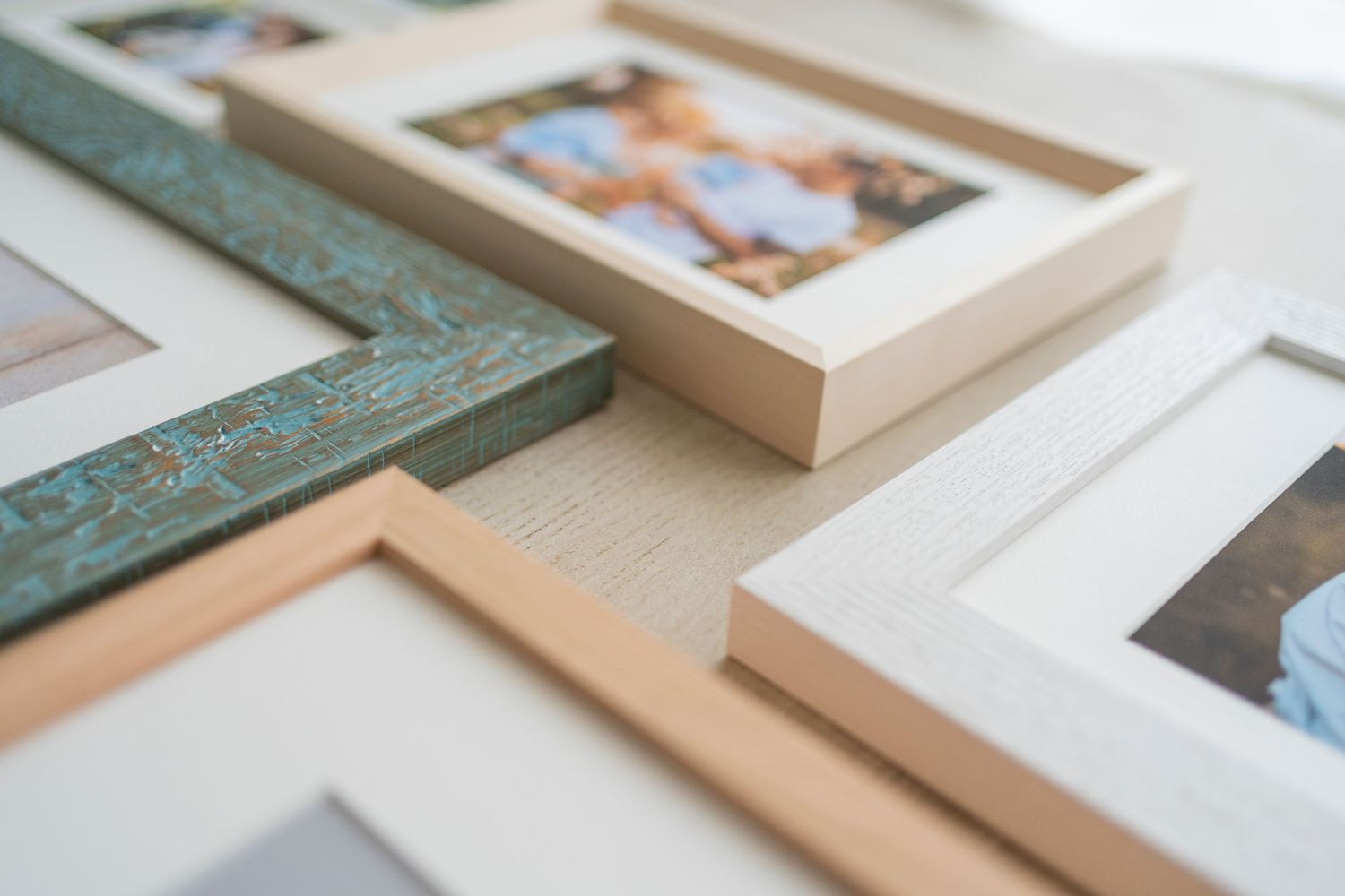 Close-up of multiple photo frames in teal, beige, and white with family photos.