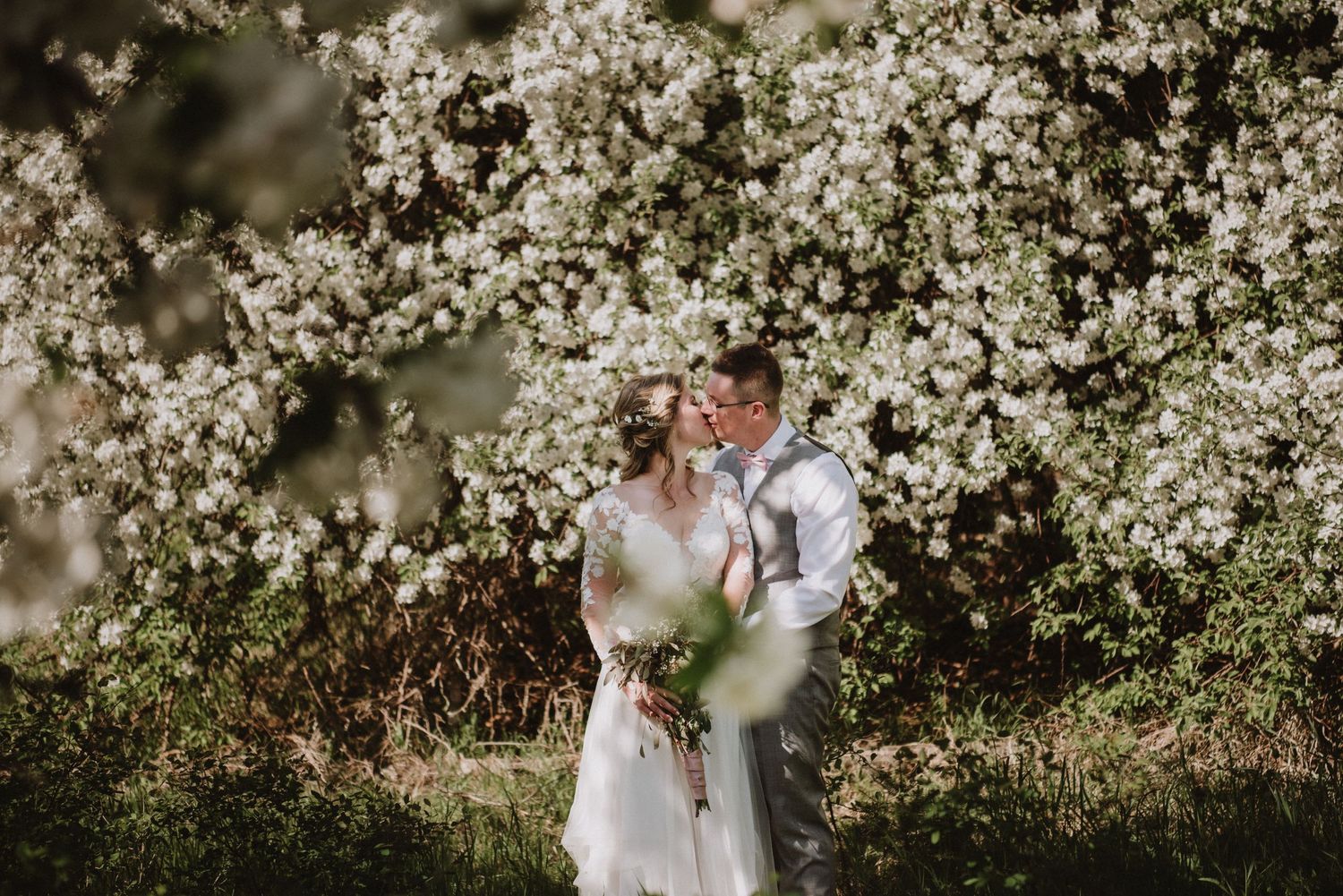 Bride and groom standing in apple orchard during their spring wedding in Salmon Arm. Photos by Kelowna photographer