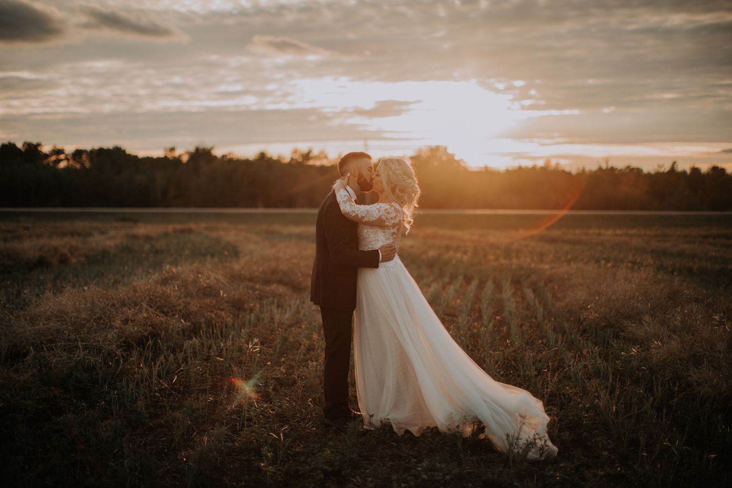 Couple embracing in a golden sunset field wearing wedding attire.