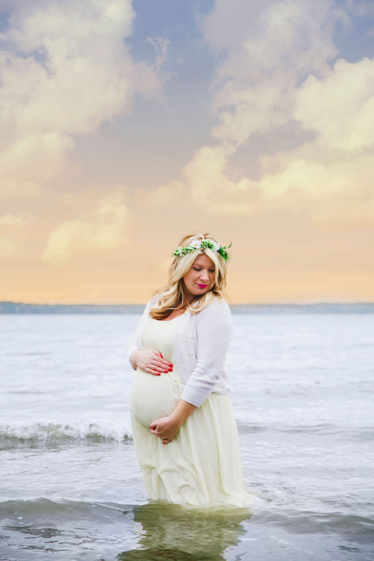 Pregnant woman with a flower crown holding belly in the water