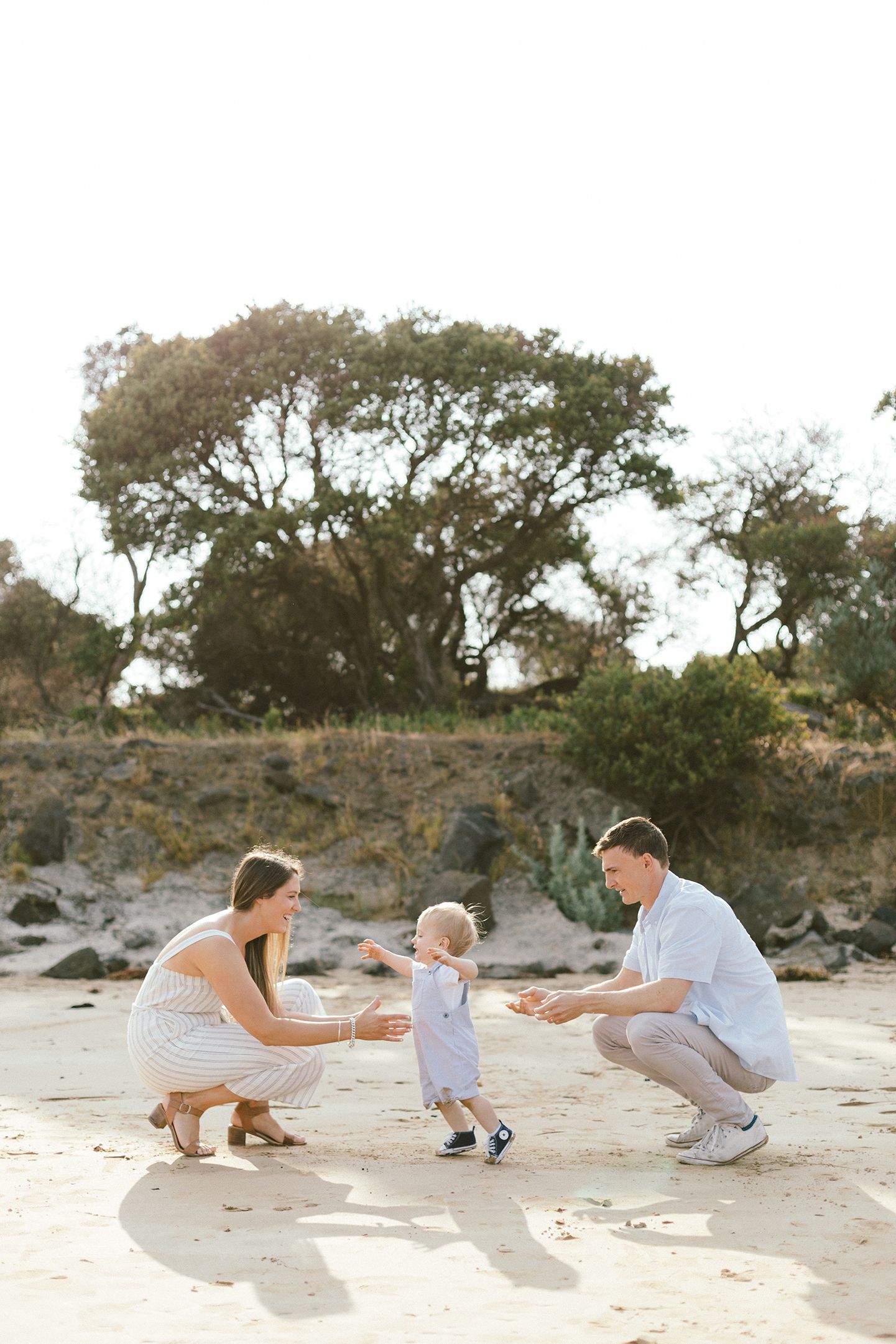 A family plays together on a sandy beach with cliffs and trees in the background.