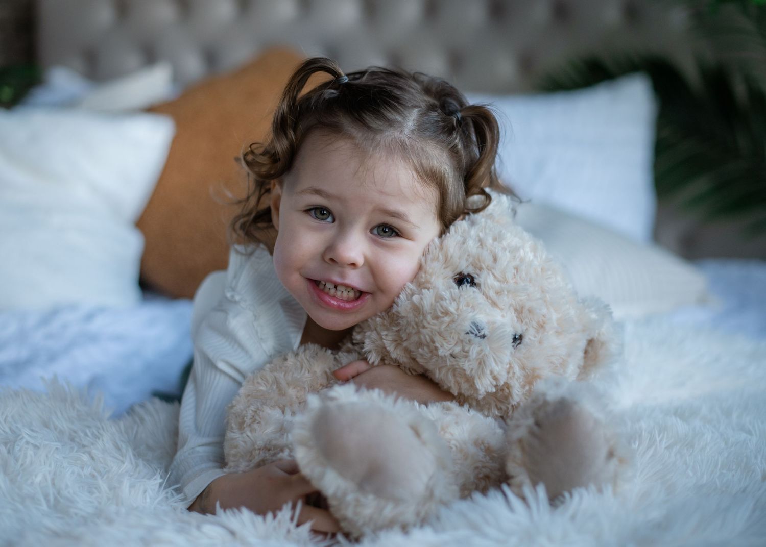 A small child hugs a teddy bear while lying on white bedding.