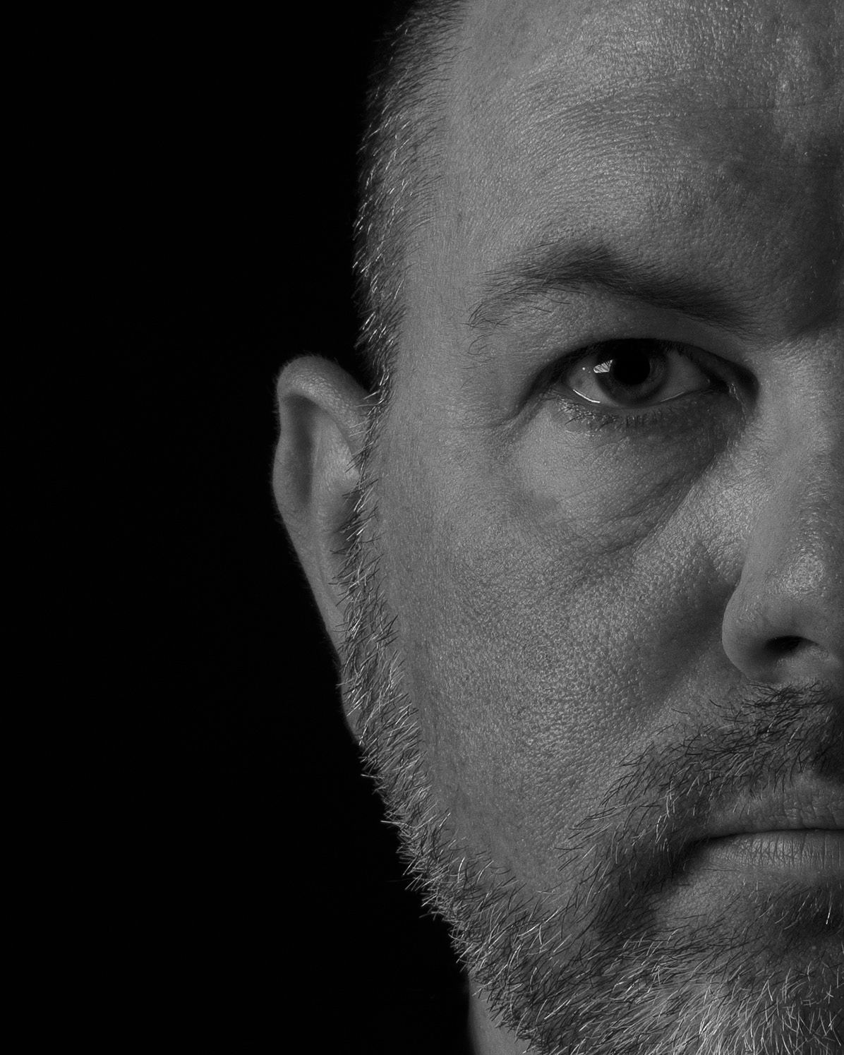 A moody black and white portrait showing the left side of a face against dark background.