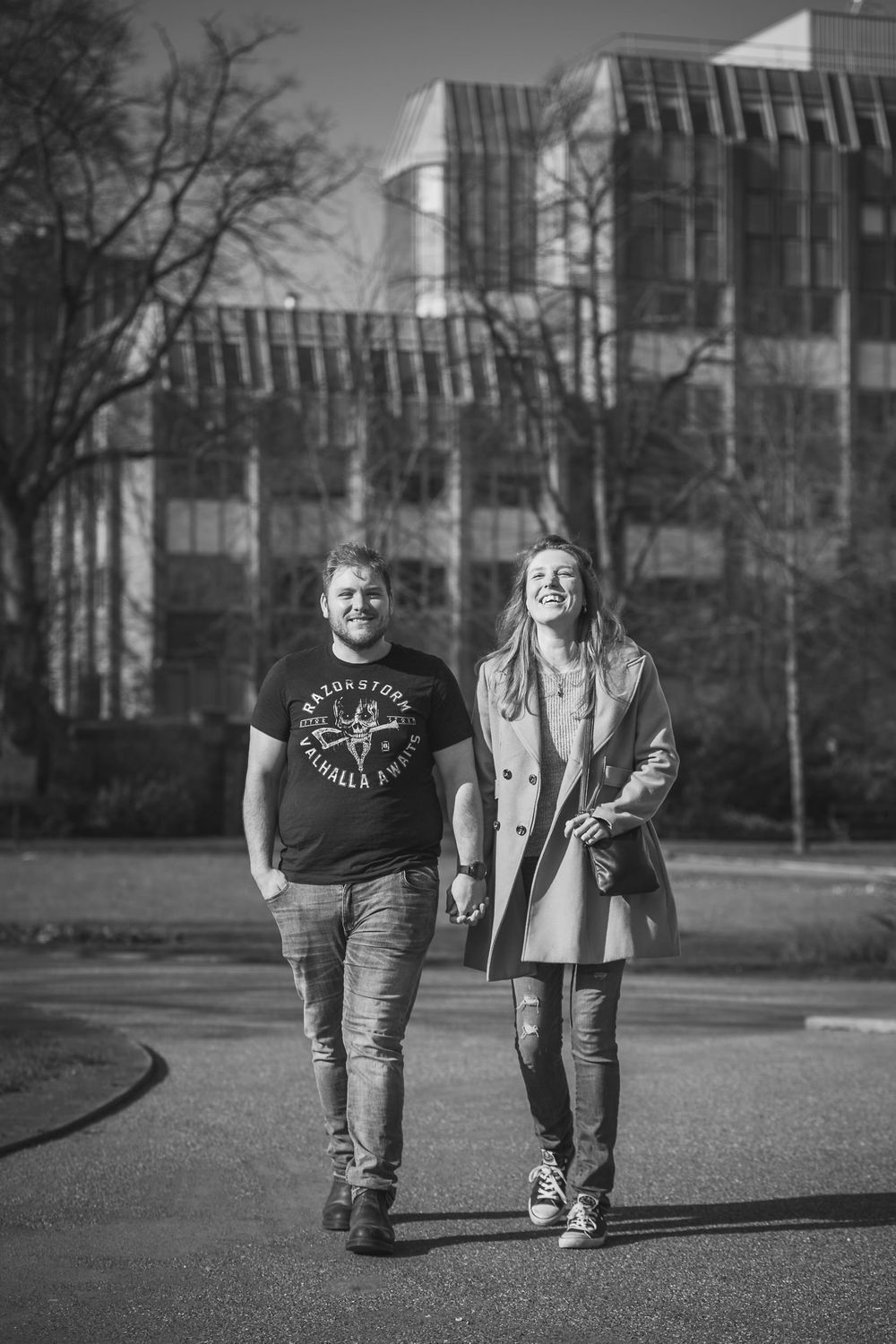 A man and woman walk happily hand in hand in a park. Laughing as they walk towards the camera.