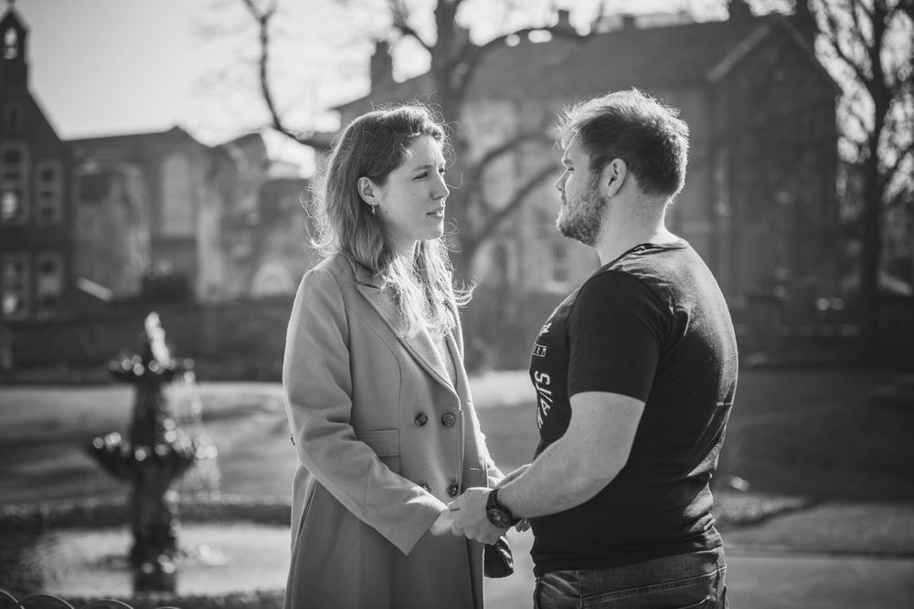 Black and white photo of a man and woman holding hands in a park, standing in front of a fountain.