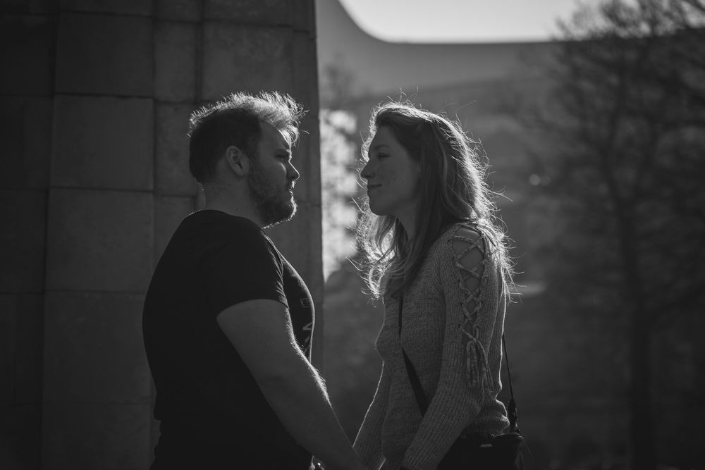 A black and white photo of a man and woman facing each other, holding hands, backlit by the sun.