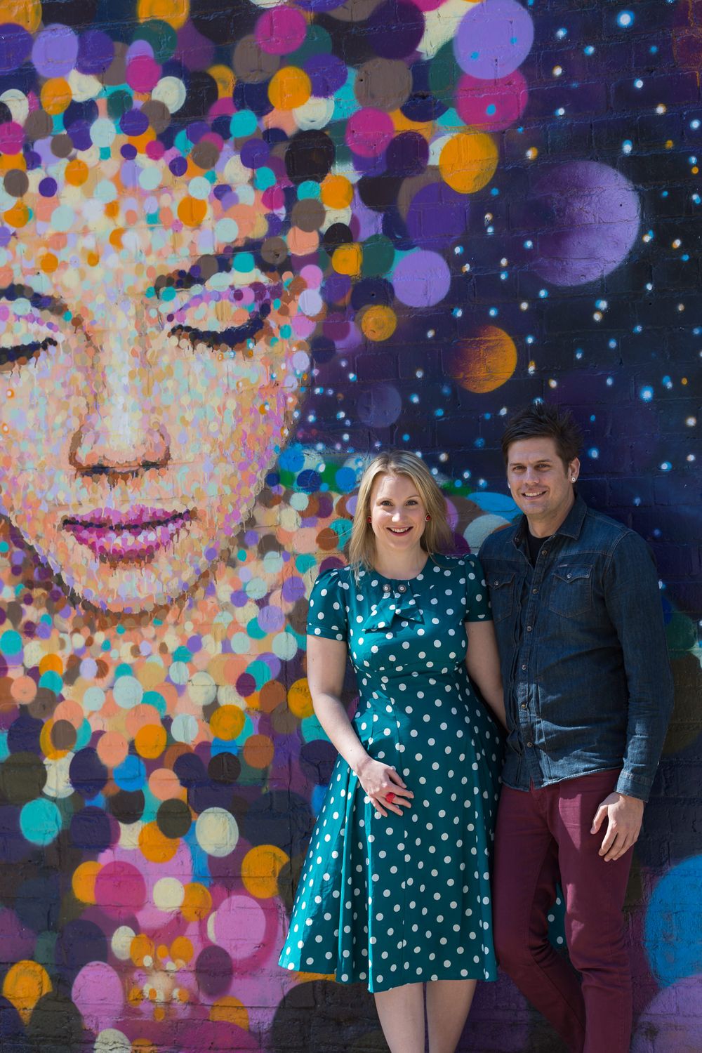 A newly engaged man and woman pose for a photo in front of some street art.