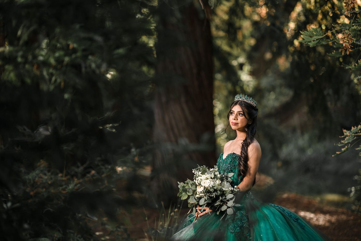 Elegant emerald ball gown with intricate details photographed in a dreamy forest setting.