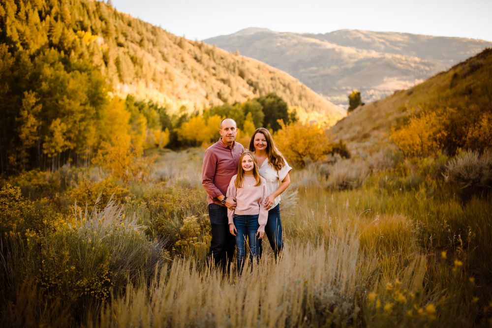 A family of three smiles with fall colors in a Vail Valley portrait