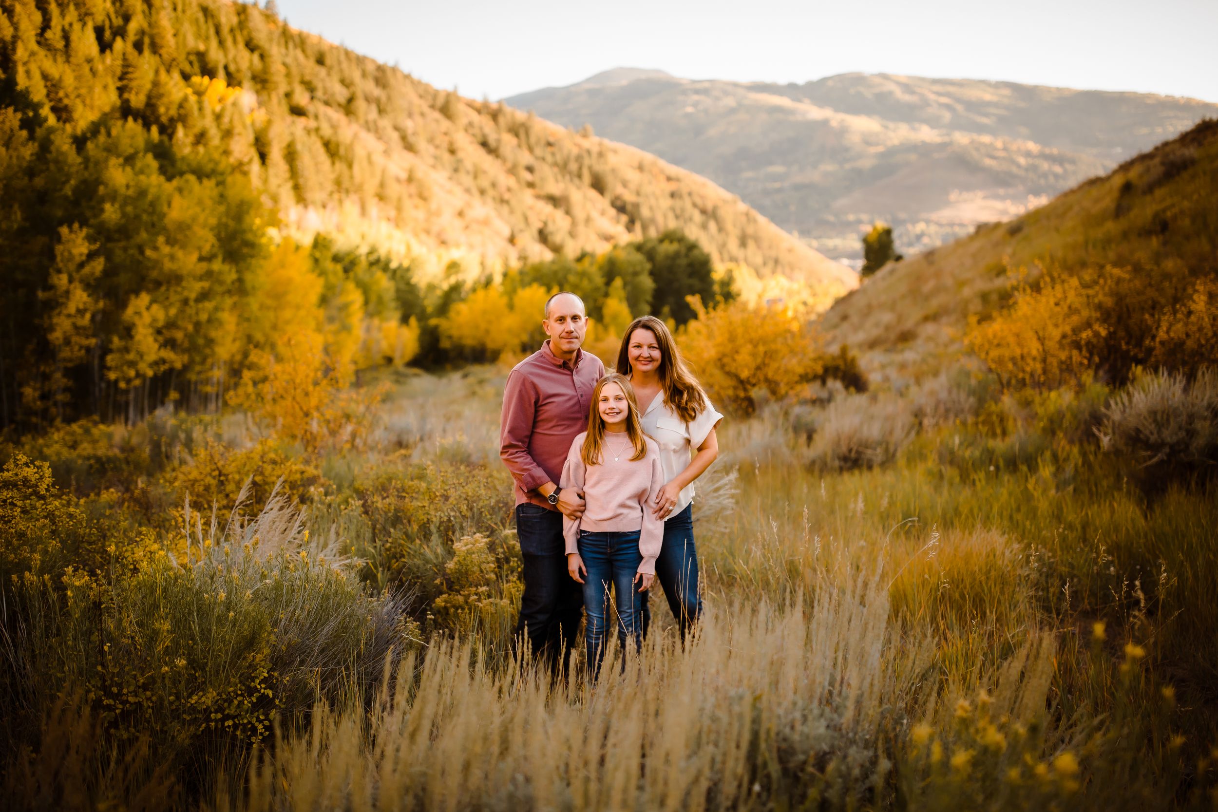 A family of three smiles with fall colors in a Vail Valley portrait