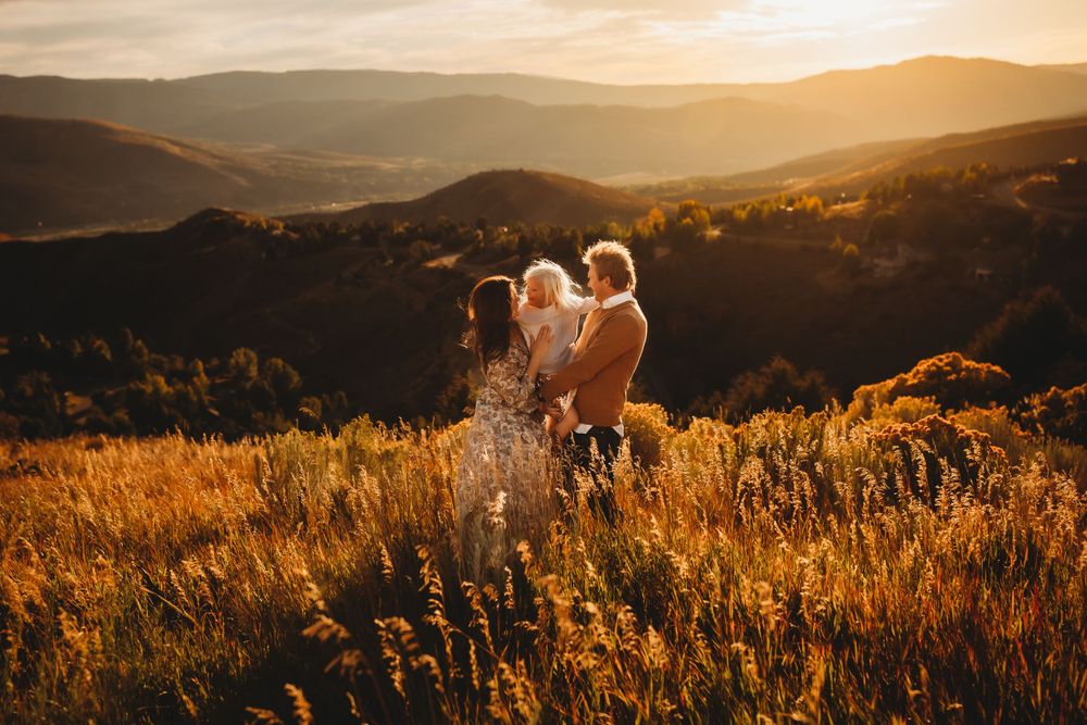 A family of three candidly smiles together at golden hour with a Vail mountain vista behind them
