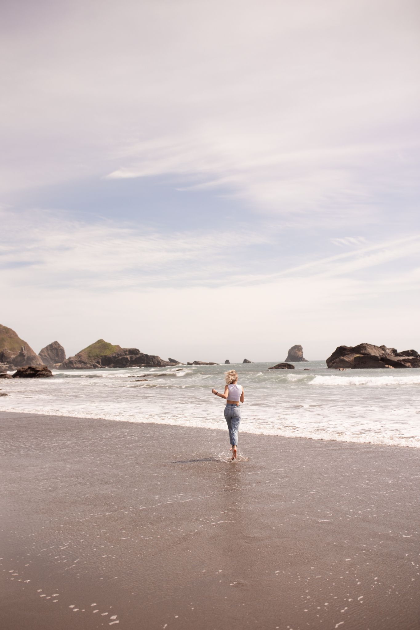 Solitary figure walking along a rocky beach shore during sunset.