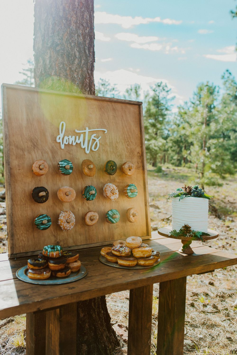 Rustic donut wall display with white cake and turquoise accents in outdoor forest setting.