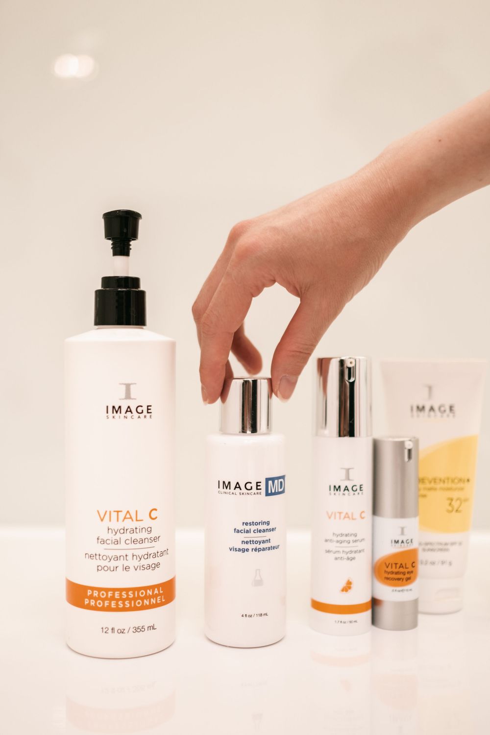 Hand reaching for Image skincare products displayed on white surface.