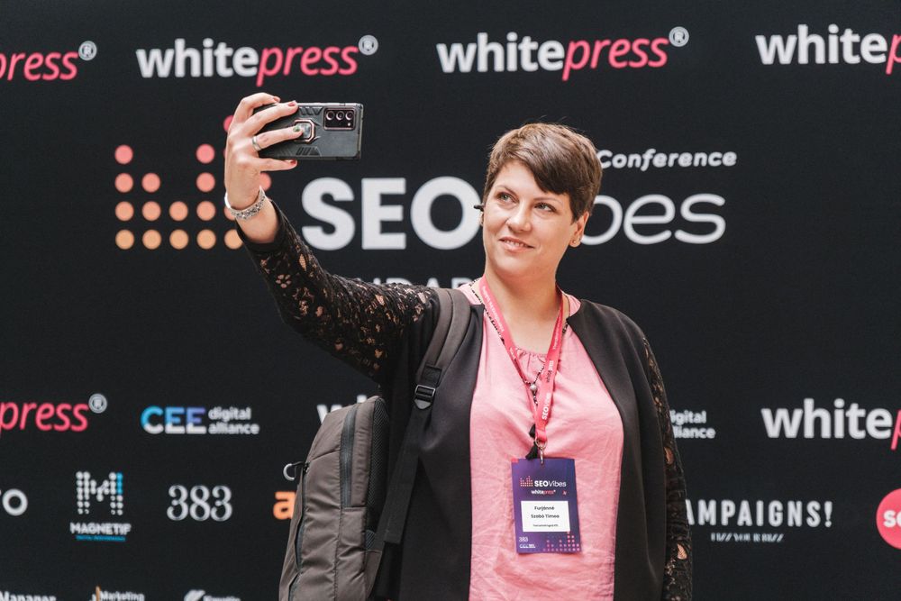 Conference attendee taking selfie at SEO event with Whitepress backdrop.