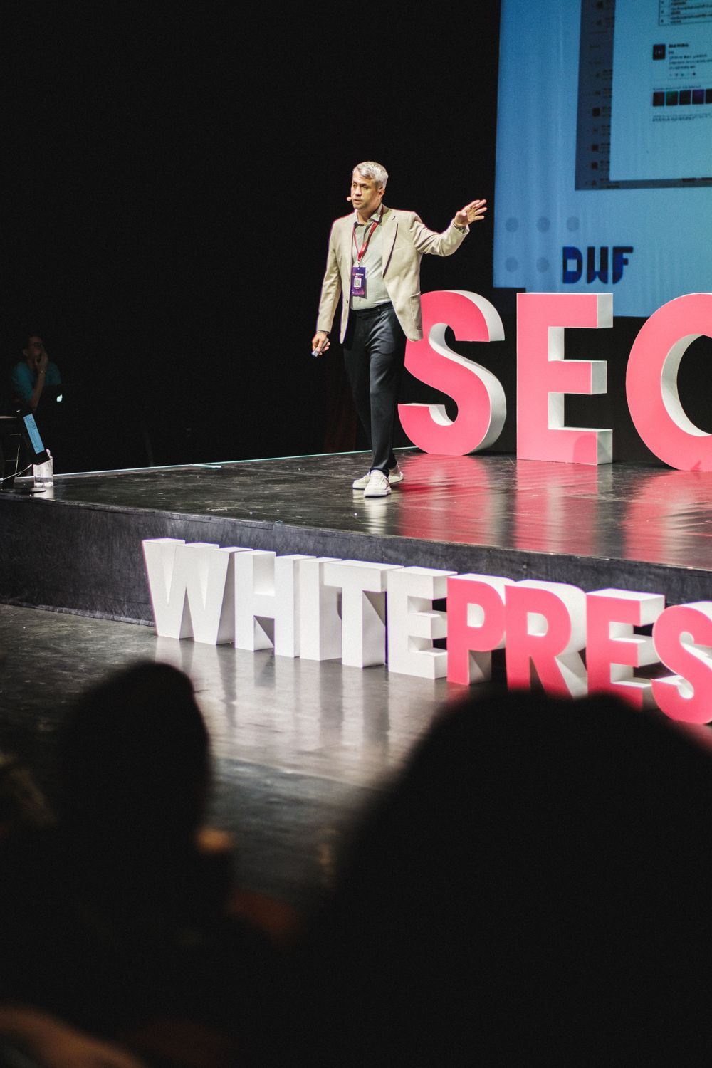 Presenter speaking on stage with large SEO and WHITEPRESS text display behind them.
