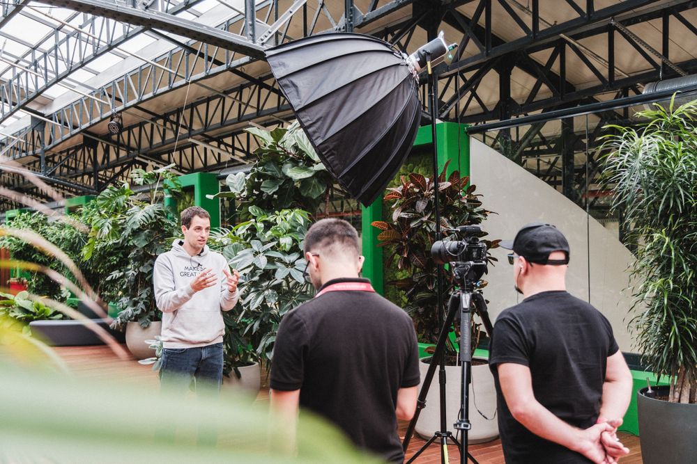 Behind the scenes of video production shoot with lighting equipment in indoor garden setting.