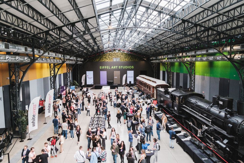 Large crowd gathering in industrial venue space with high glass ceiling during conference event.