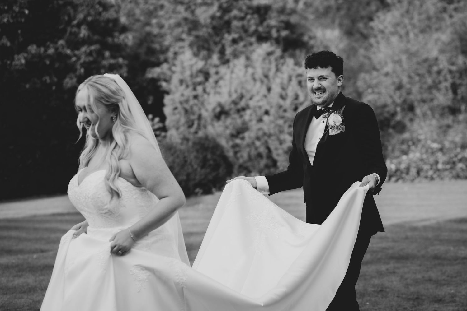 A playful black and white wedding photo of a couple with the bride's dress flowing in the wind.