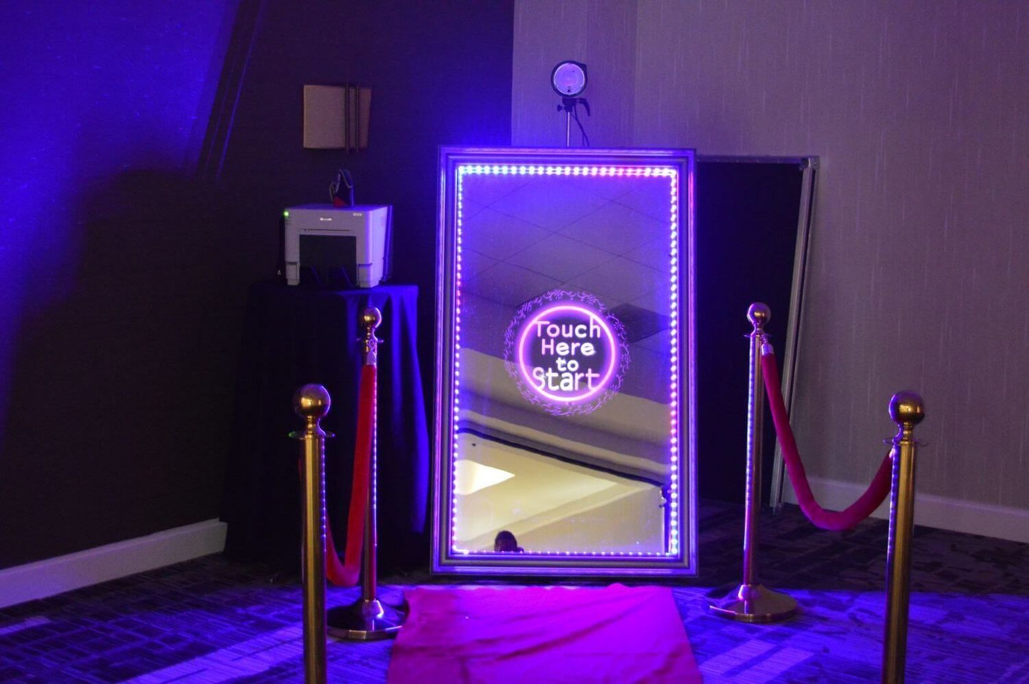 Illuminated LED magic mirror photo booth with red velvet ropes at a wedding or event venue.