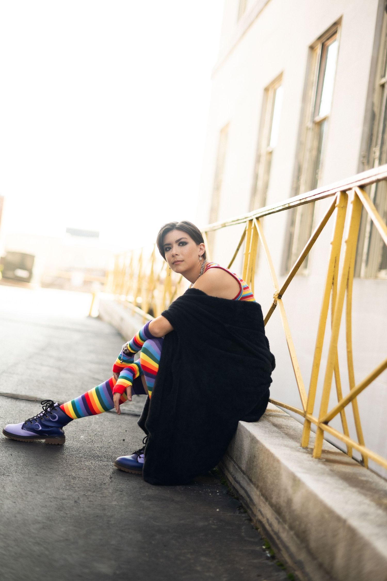 Urban fashion scene with rainbow striped socks contrasting against a black outfit and industrial background.