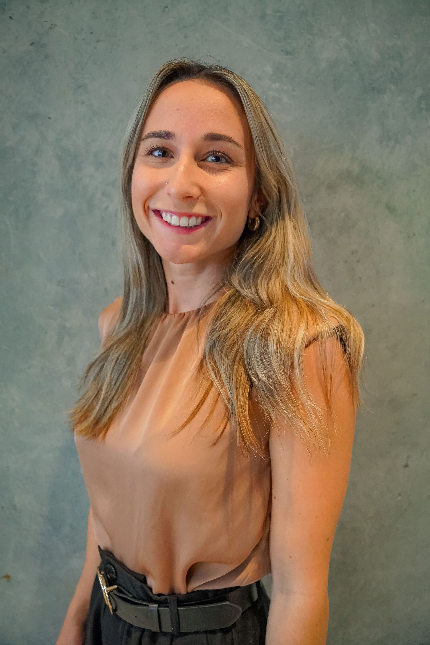Professional portrait of someone wearing a beige top against a textured gray background.