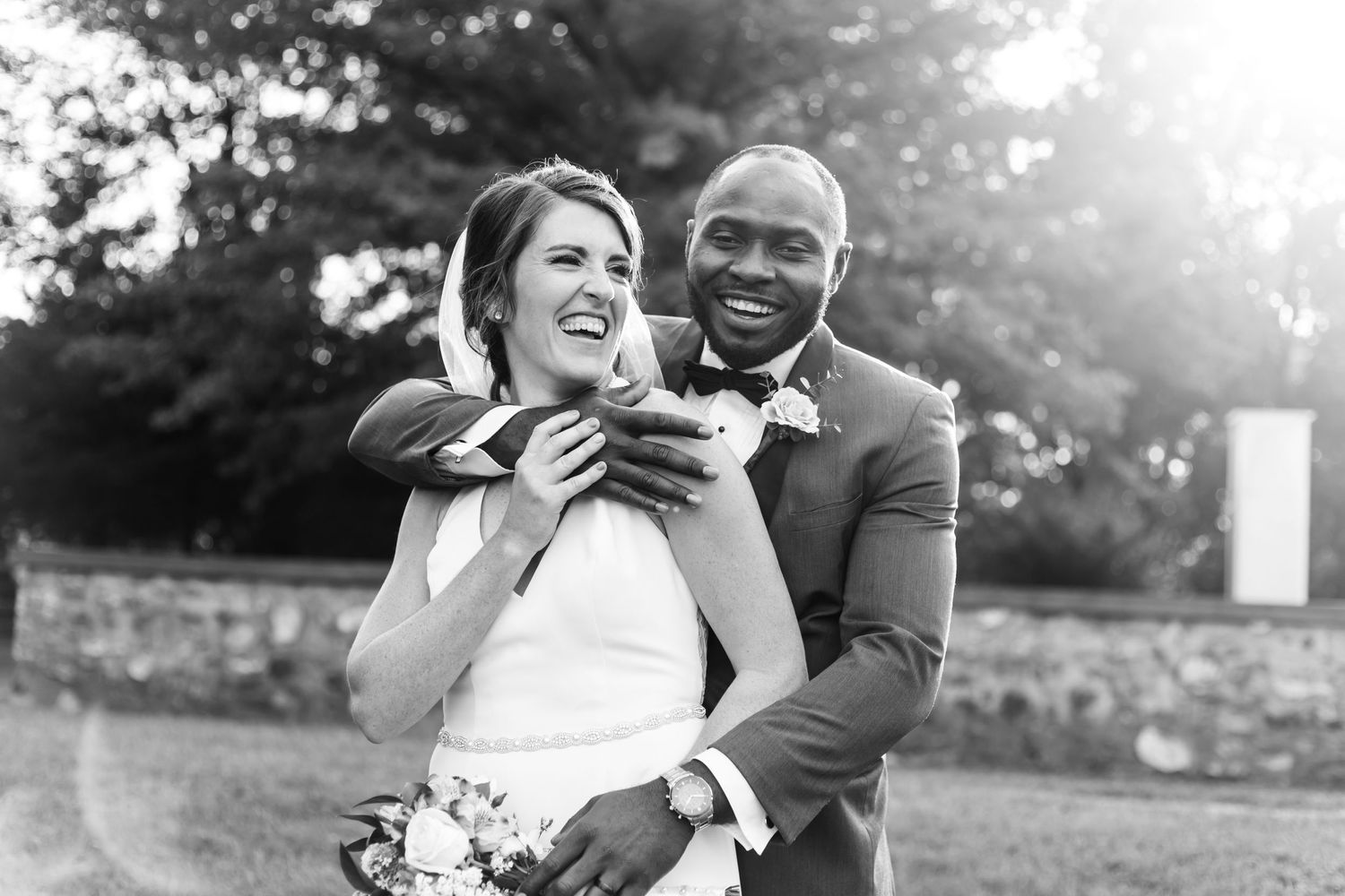 Black and white candid wedding photo capturing laughter and embrace between newlyweds.