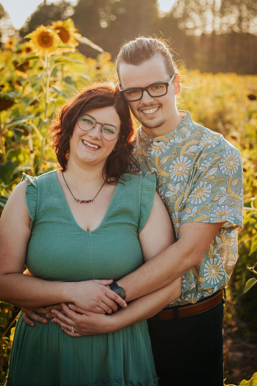 A couple poses in a sunflower field at sunset wearing coordinated casual outfits.