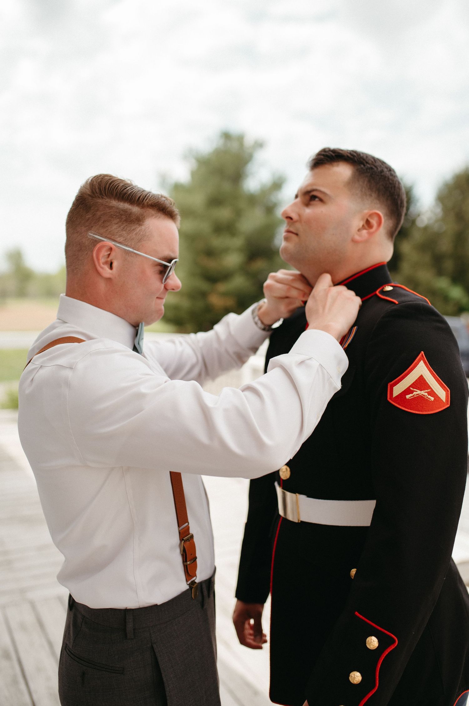 Military uniform being adjusted before ceremony on outdoor deck.