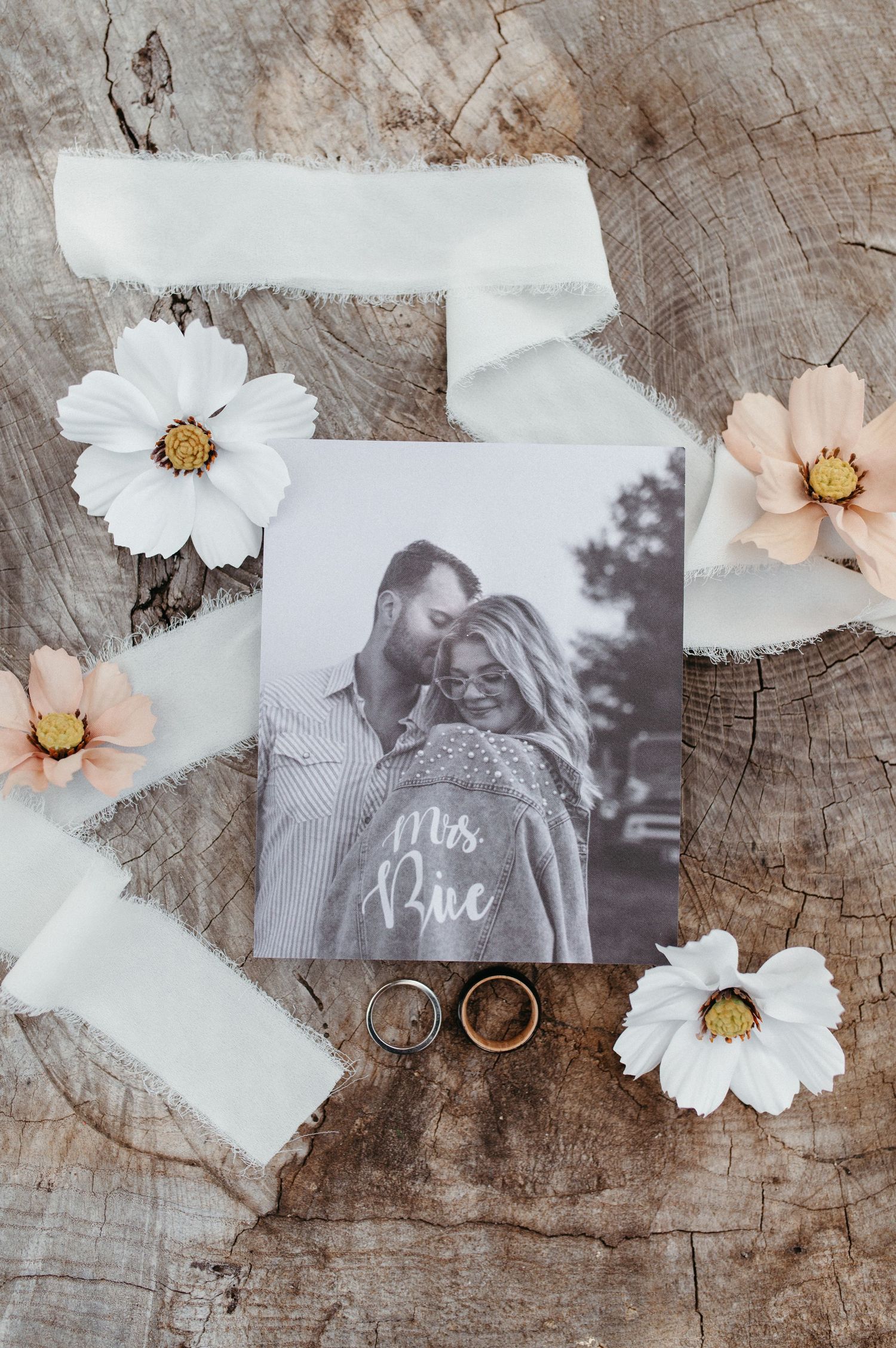 Wedding rings with flowers and a photograph arranged on weathered wood.