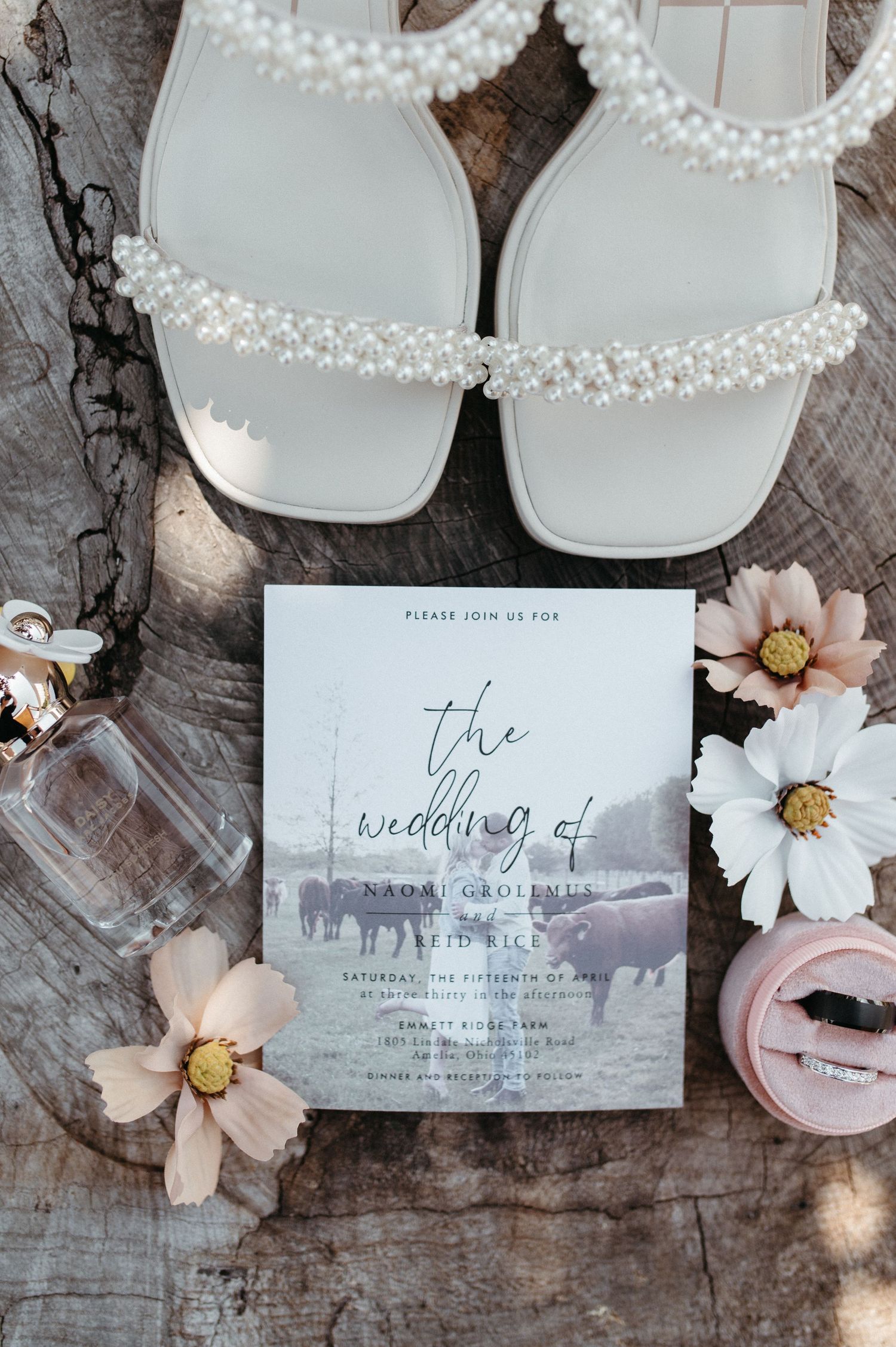Elegant wedding invitation with white sandals and delicate flowers on wooden surface.