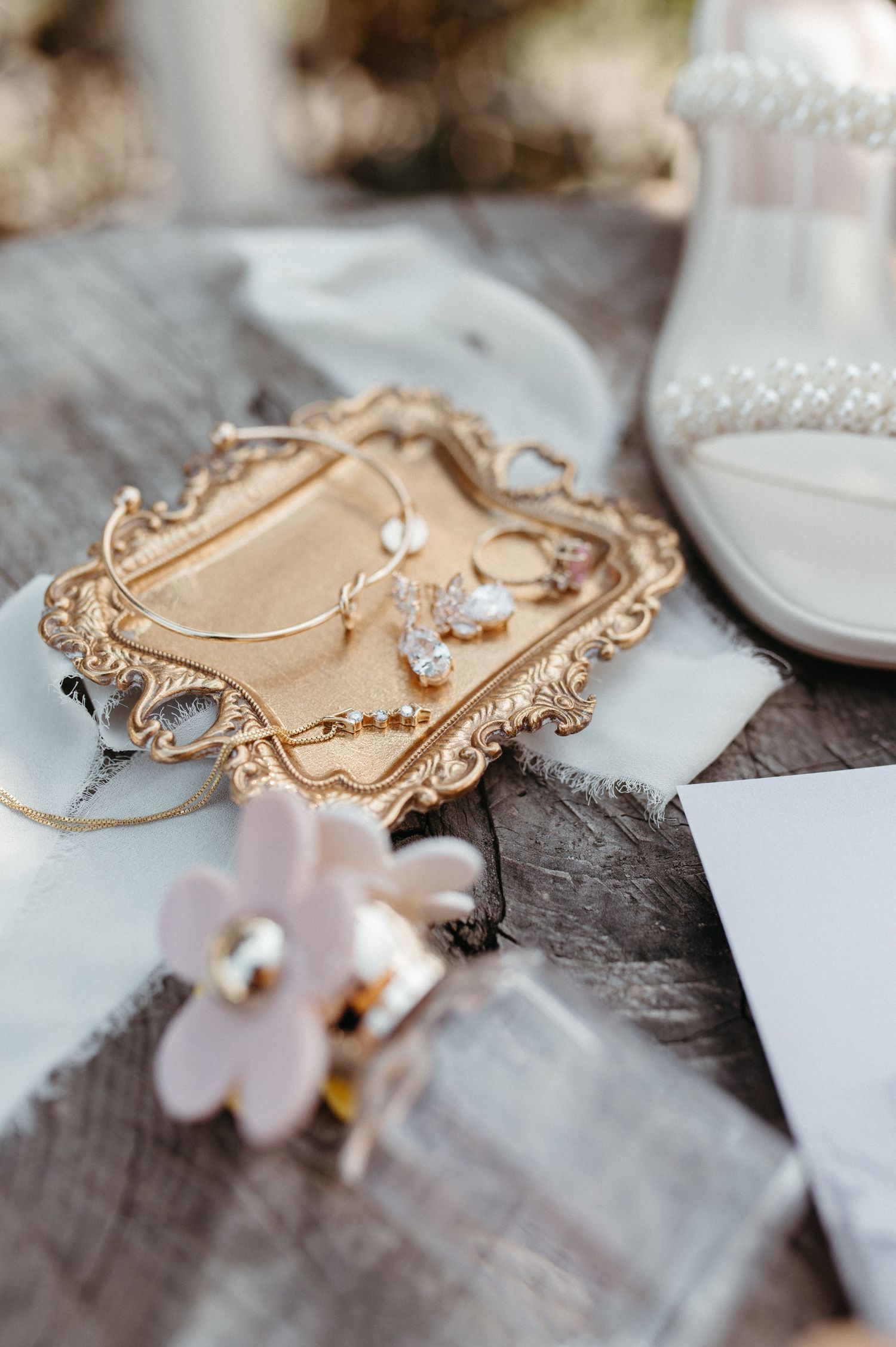 Vintage gold tray with jewelry and delicate flowers on rustic wood background.