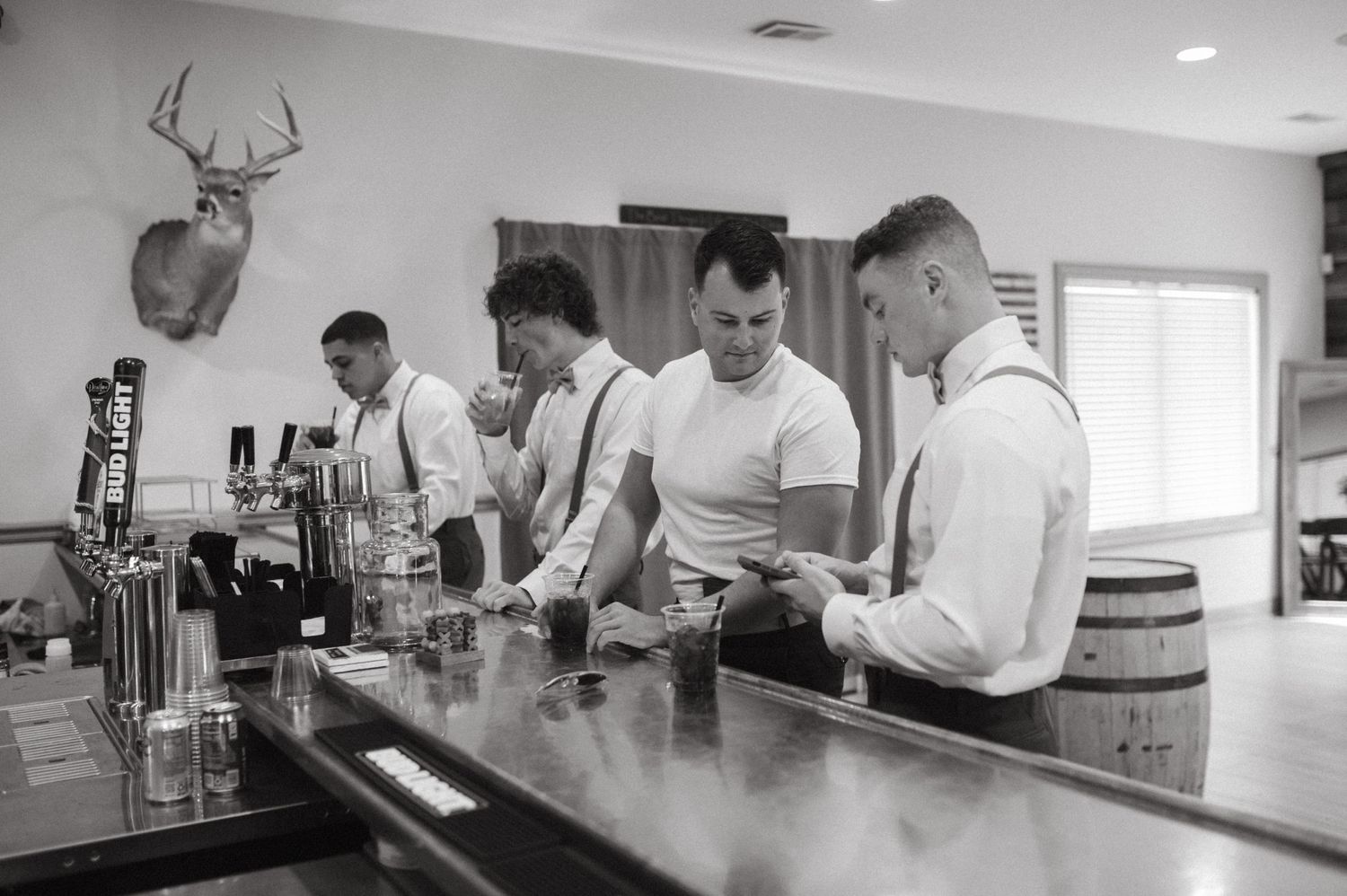 Bartenders preparing drinks at rustic bar with mounted deer head on wall.