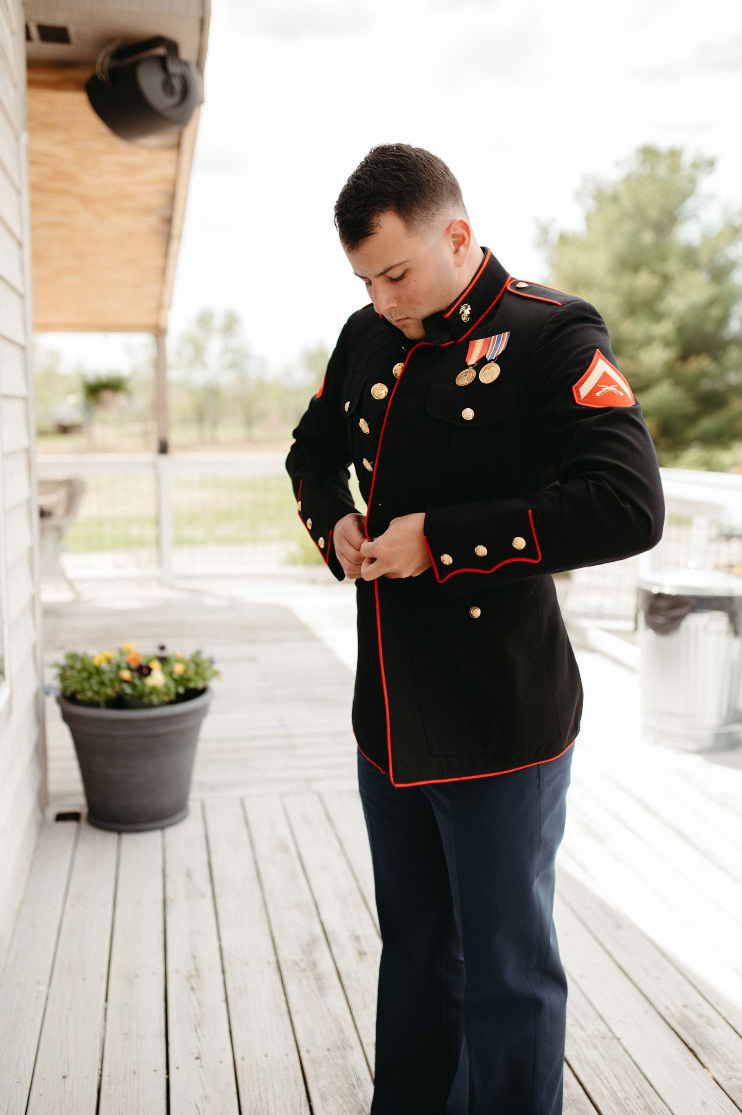 Marine in dress blues adjusting uniform on outdoor deck.