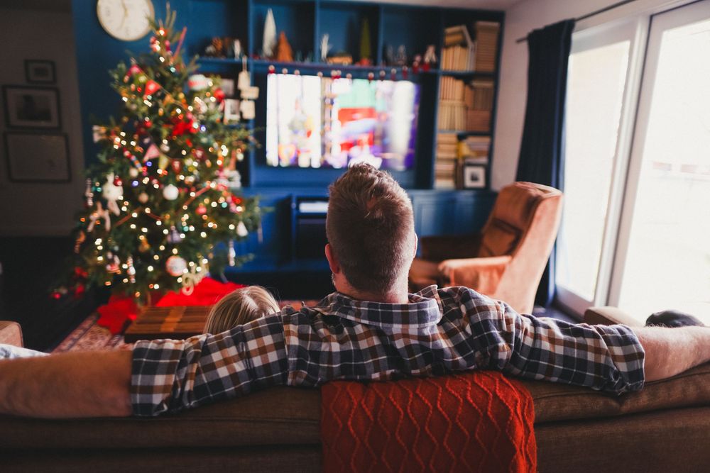 Living room decorated for Christmas with a lit tree and TV in the background.