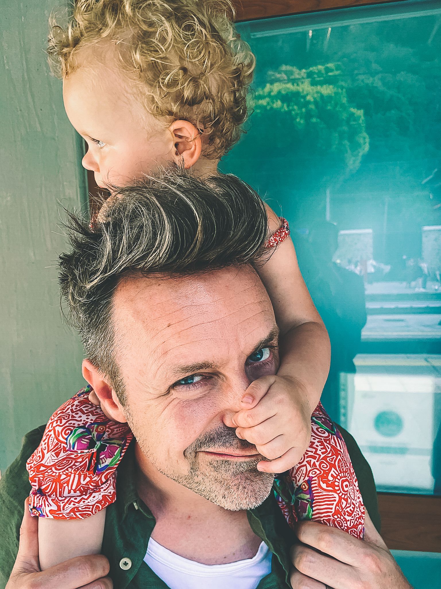 A playful moment captured with someone being held on shoulders against turquoise background.