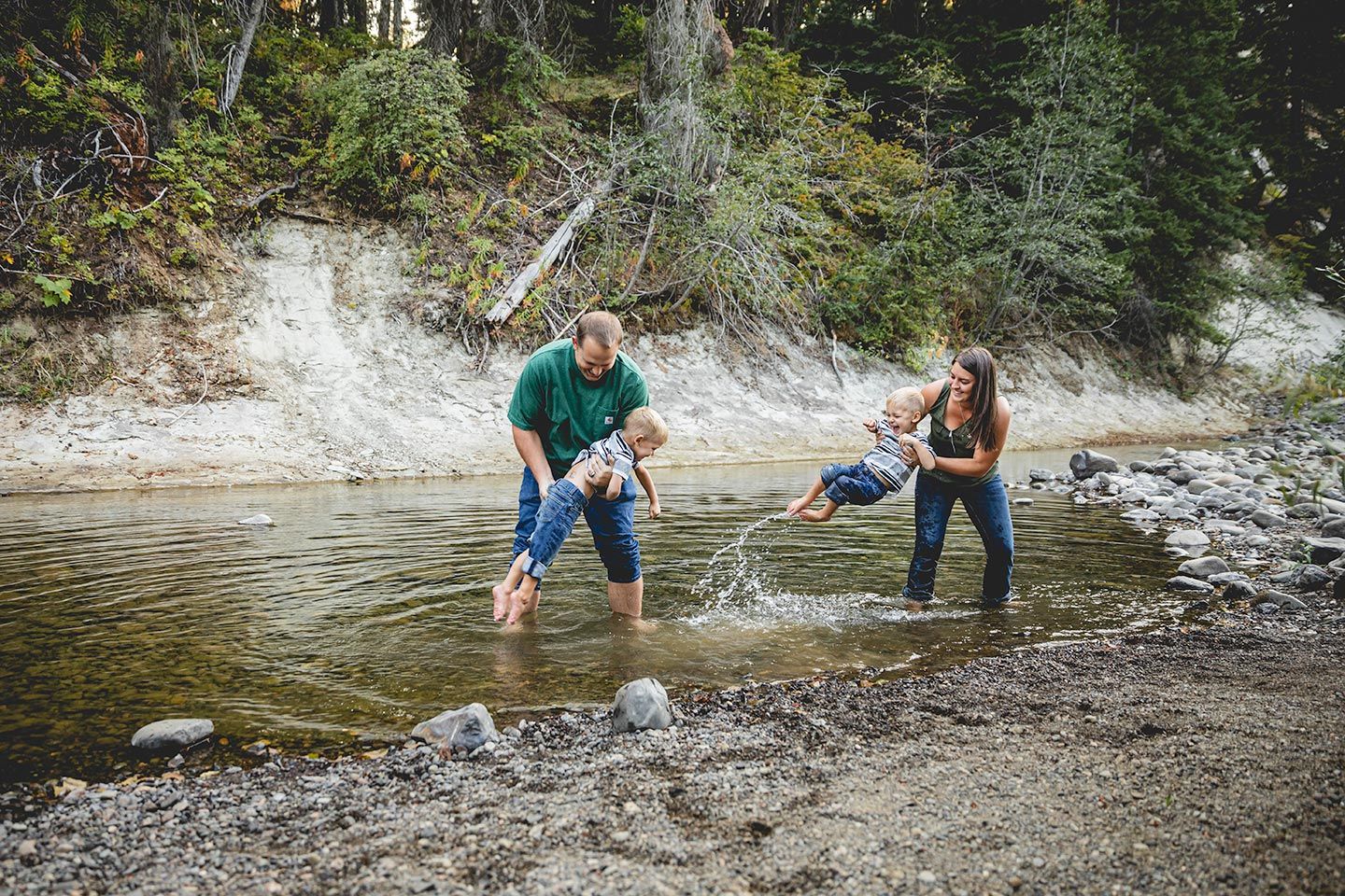 parents each holding one of their twin sons and splashing their feet in the teannaway river