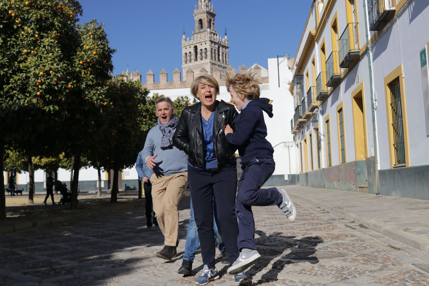 People jumping and playing together on a sunny street with historic architecture and church tower in the background.
