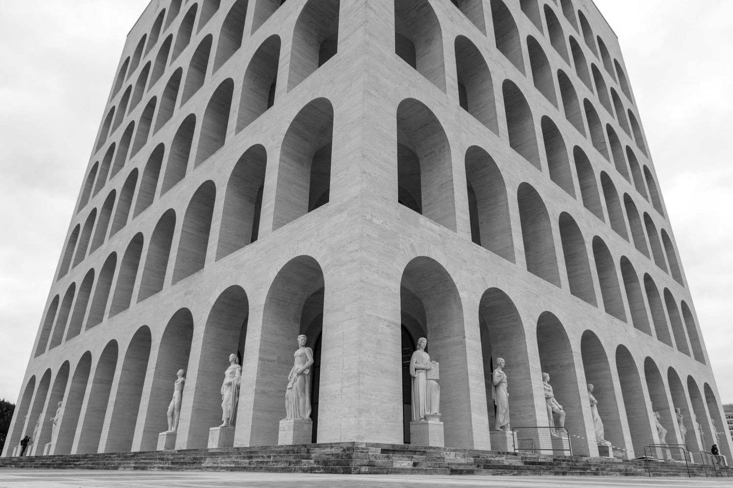 Dramatic black and white architectural detail of a modernist building featuring repetitive arched columns and openings.