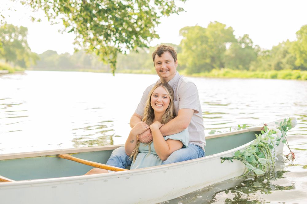 Couple sitting together in a canoe on a calm lake surrounded by lush green trees.