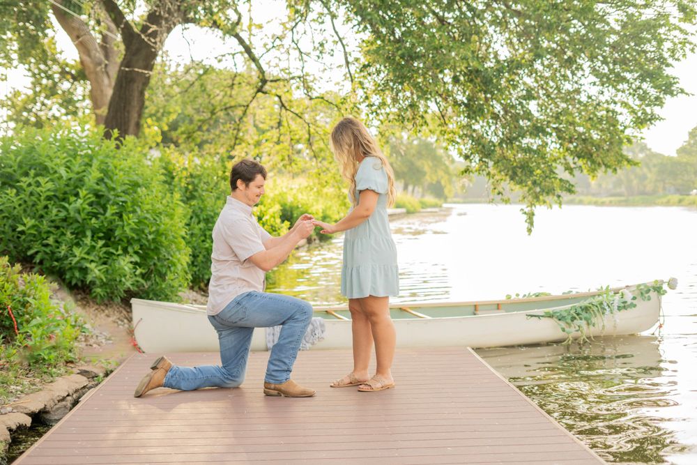 Romantic marriage proposal on a wooden dock by a lake, man on one knee presenting a ring to his partner.