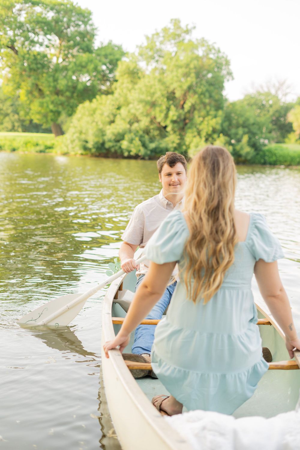 Couple rowing a white canoe on a peaceful lake, man smiling at his partner on a sunny day.