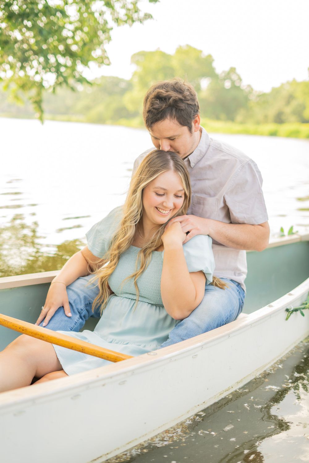 Romantic couple embracing in a canoe on a sunlit lake with golden light filtering through trees.