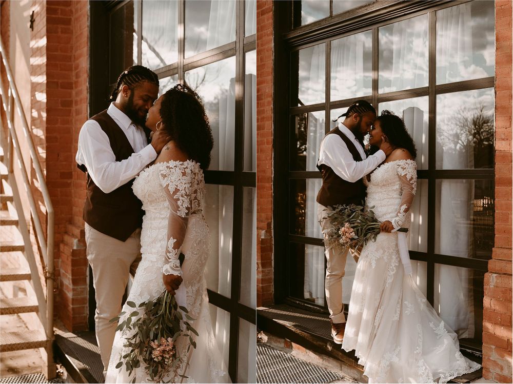 Romantic wedding couple poses by large industrial windows in vintage venue.