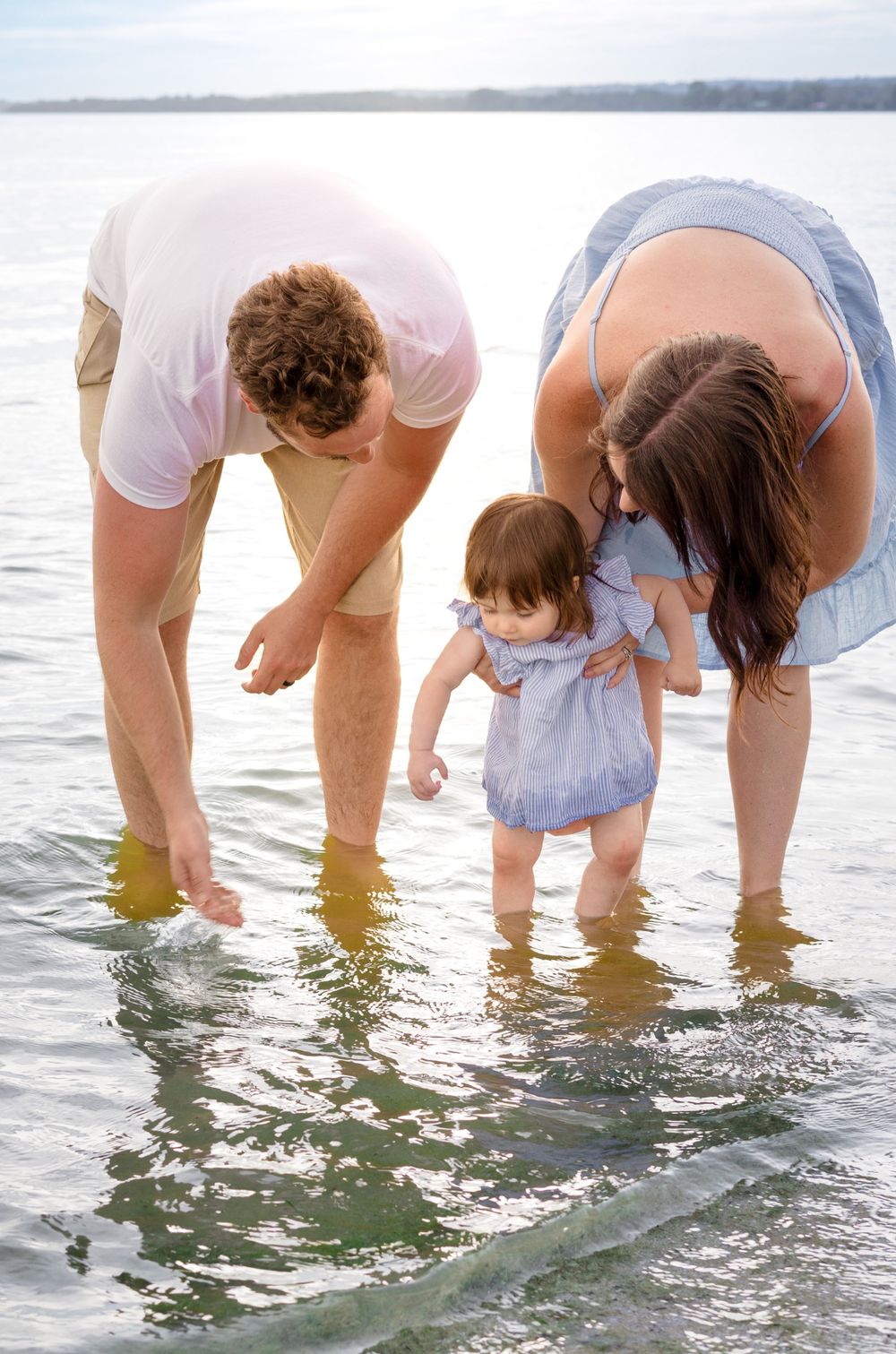 Family bending down to touch water together at beach edge.