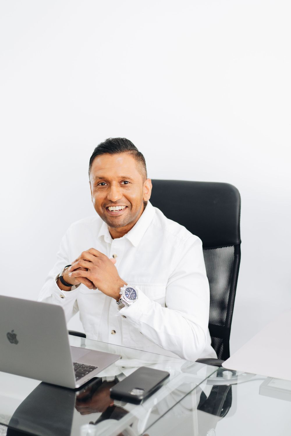 Professional in white shirt working at glass desk with laptop and accessories.