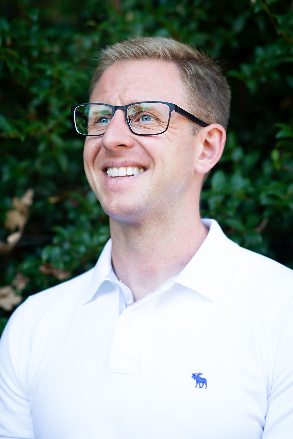 Professional headshots in white dress shirt against natural green background.