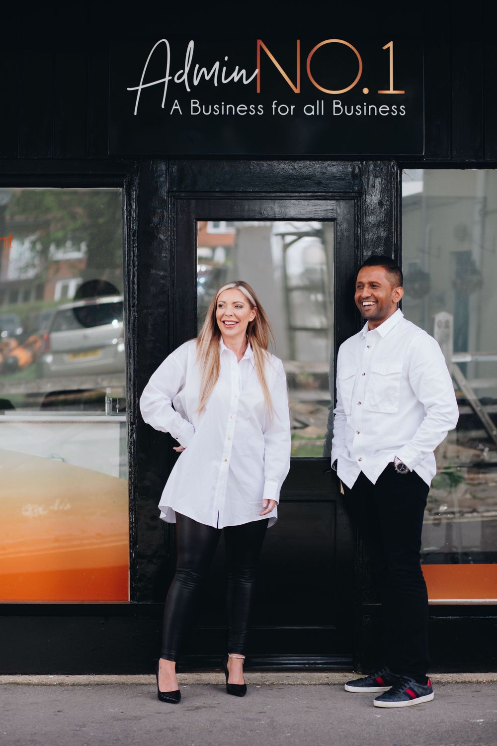 Professional business storefront with white-clad people standing outside a black building with orange accents.